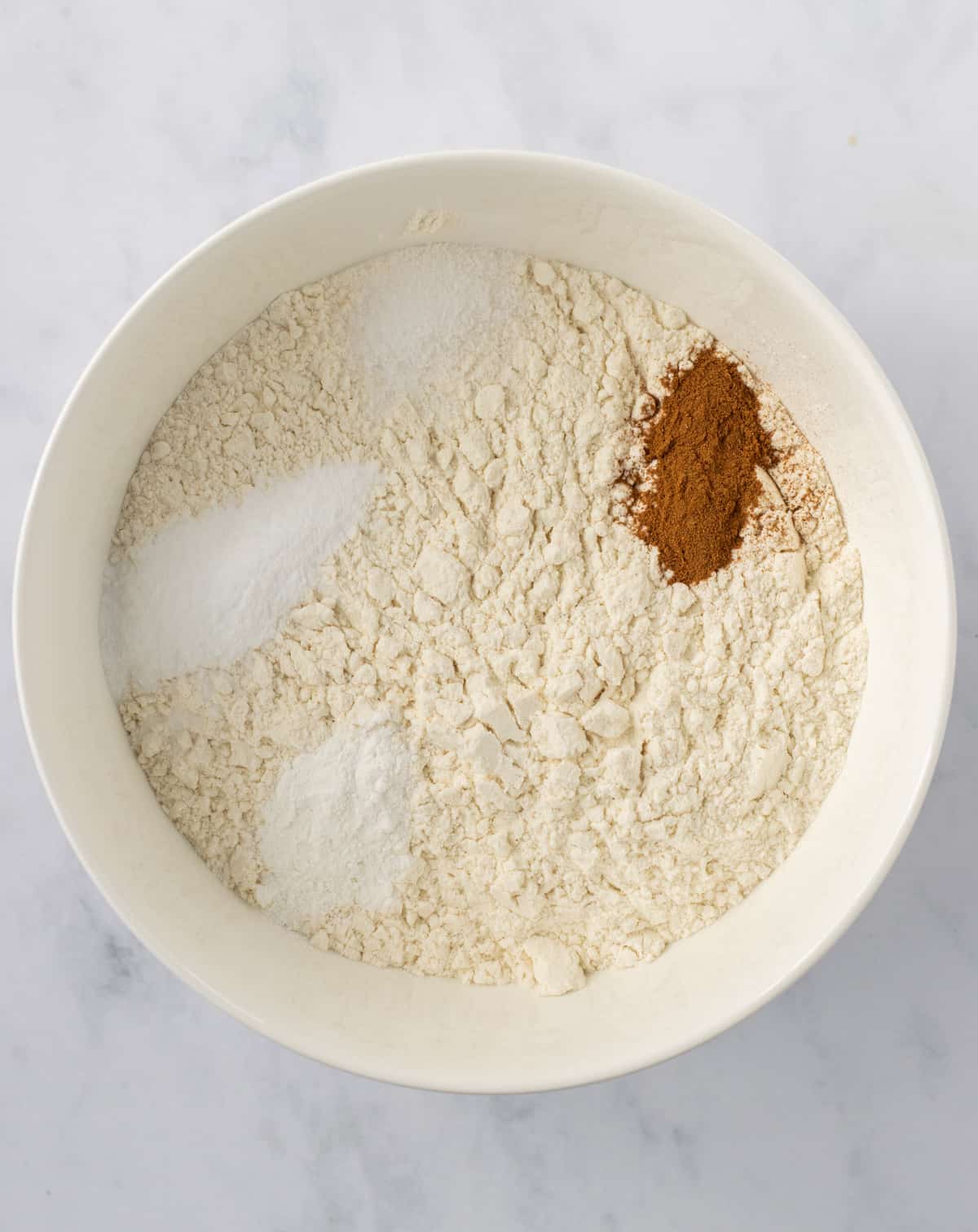 Flour, baking soda, baking powder, salt, and cinnamon in a bowl.