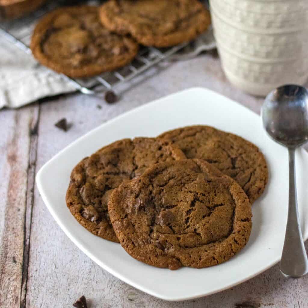 Three coffee cookies on a plate with a spoon next to a coffee mug.