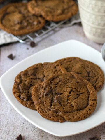 Three coffee cookies on a plate with a spoon next to a coffee mug.