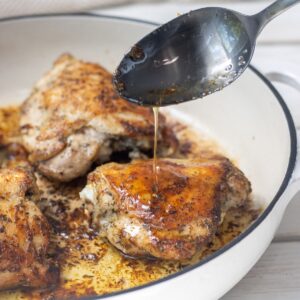 Chicken thighs in a casserole pan with butter sauce being poured over one of them.