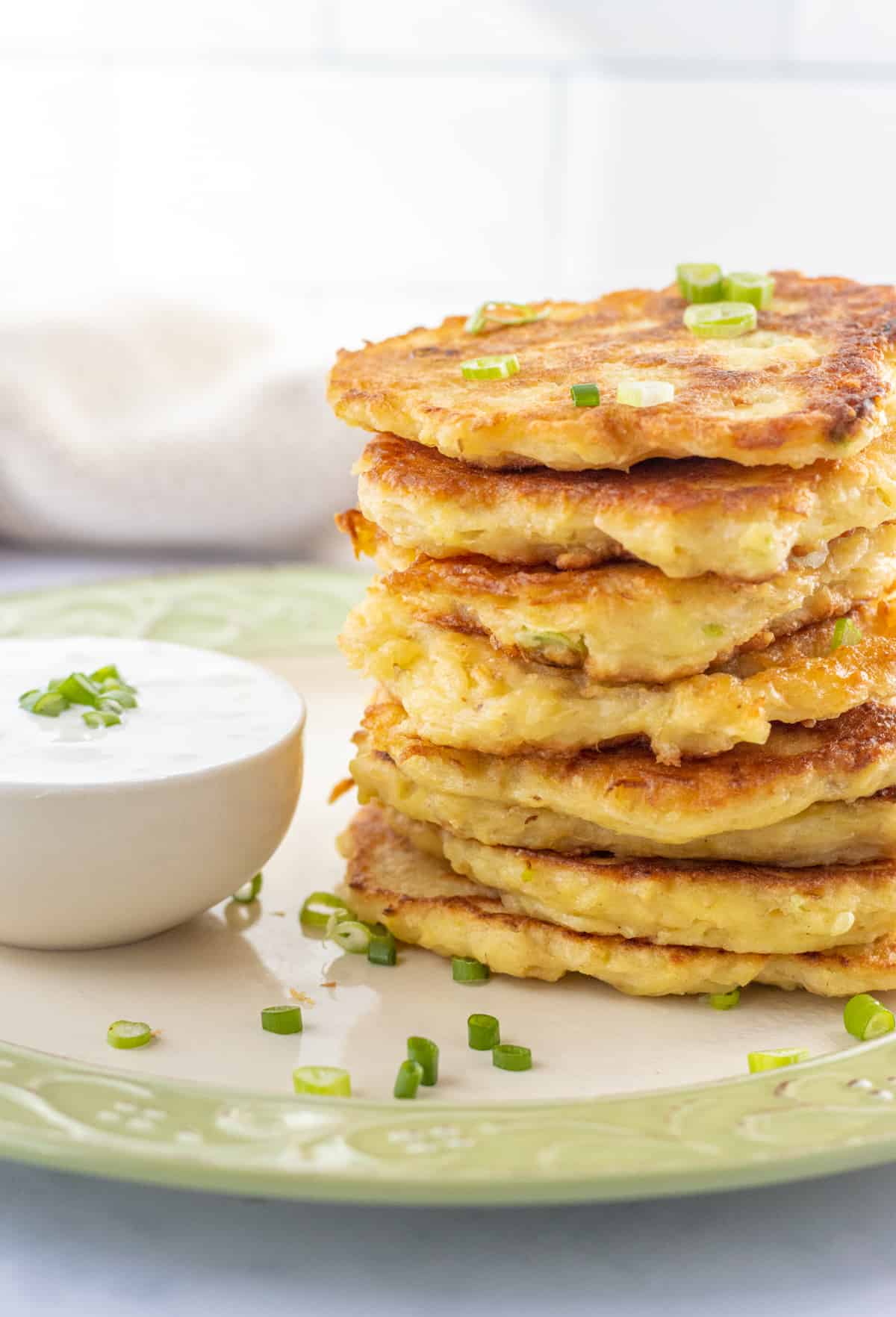 Stack of potato fritters on a plate next to a bowl of sour cream.