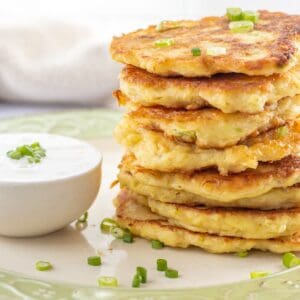 Stack of potato fritters next to a bowl of sour cream.