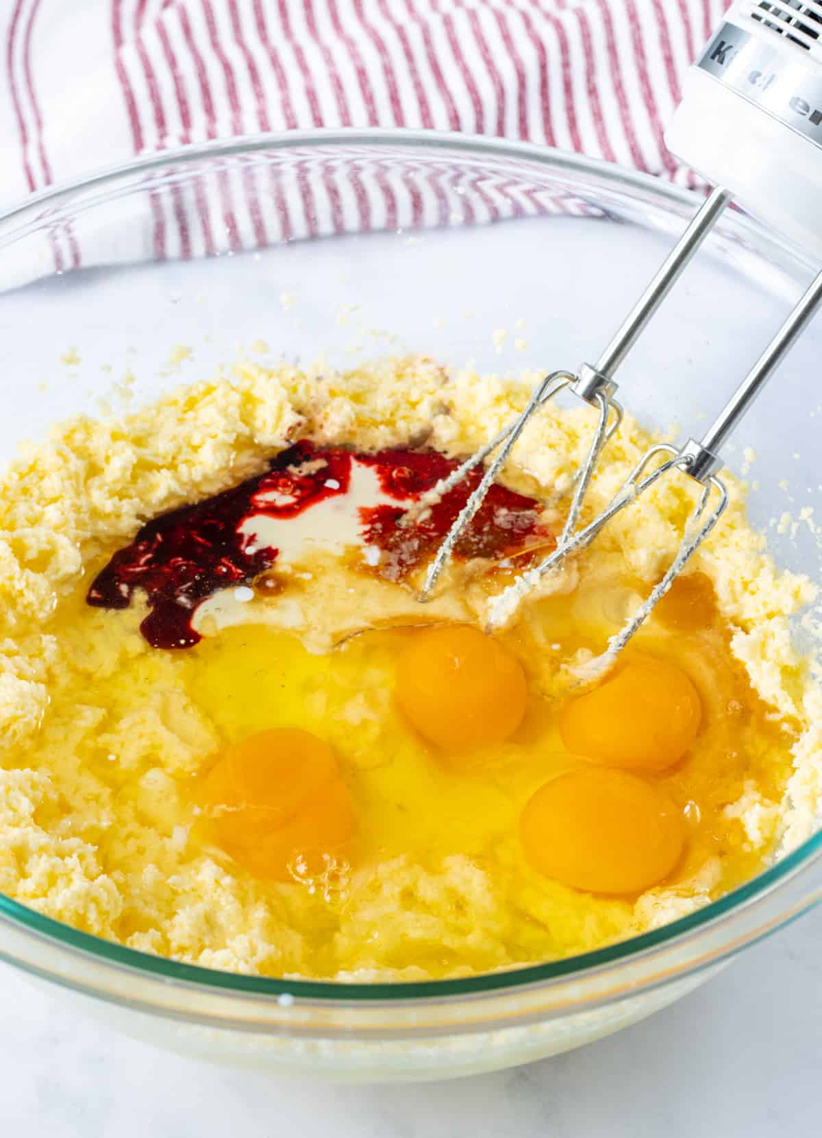 Creamed butter and sugar, buttermilk, eggs, vanilla, vinegar, and red food dye in a bowl.