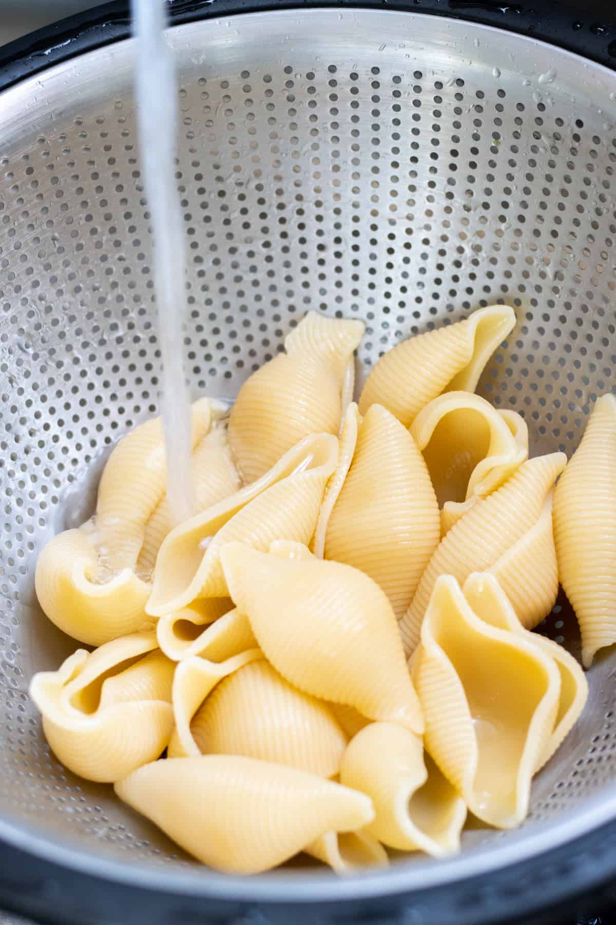 Shell pasta in a colander being rinsed with water. 