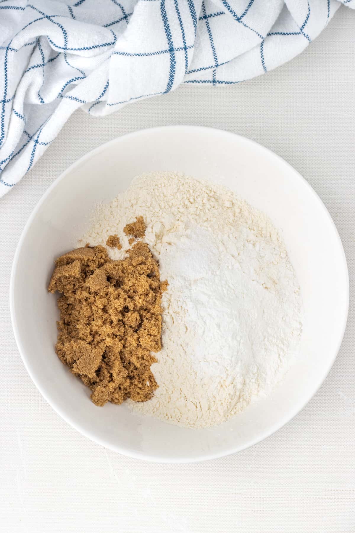 Flour, brown sugar, baking powder, and salt in a bowl next to a towel.