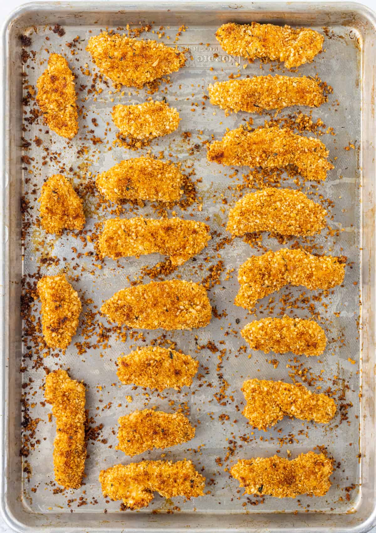 Breaded chicken strips baked on a baking sheet.