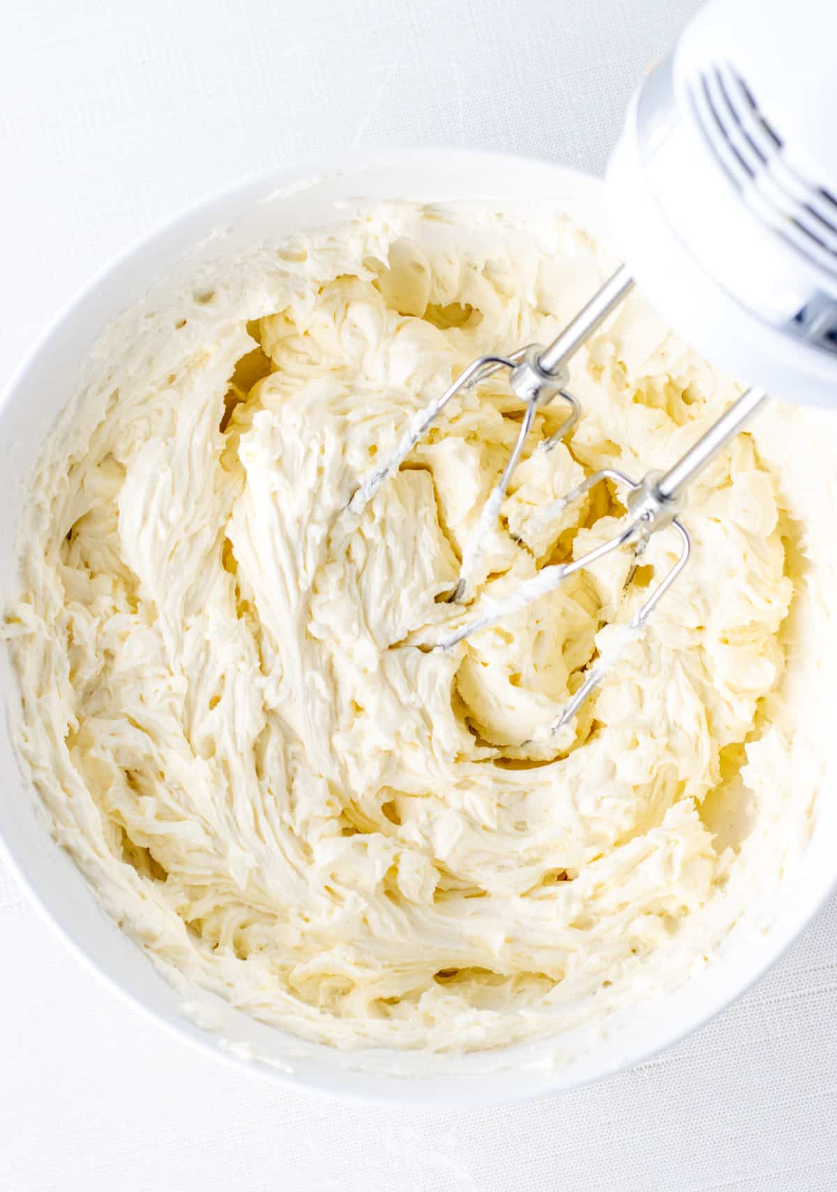 Mascarpone frosting in a bowl with and electric whisk on the side.