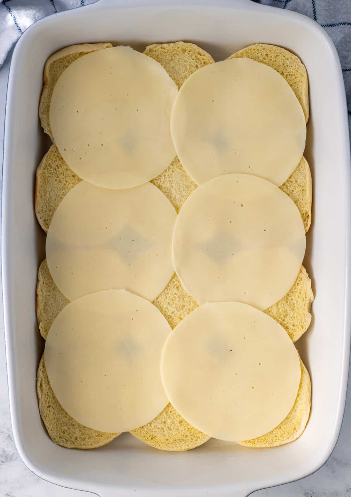 Bun bottoms with slices of provolone cheese covering them.