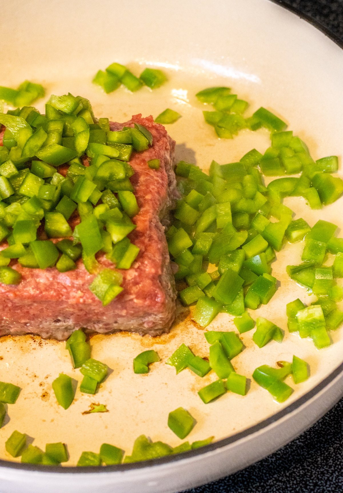 Ground beef and diced green peppers in a skillet.