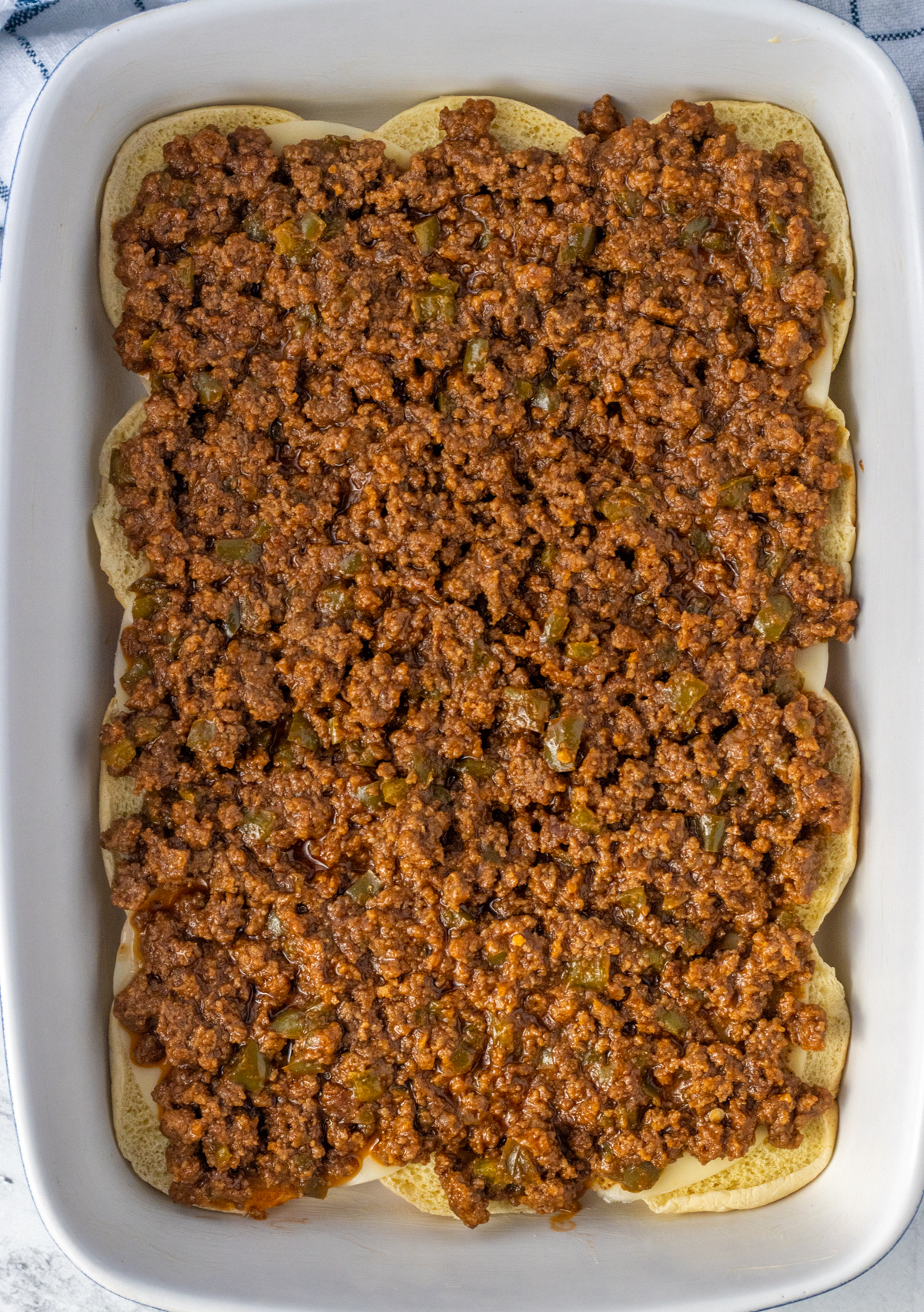 Cooked sloppy joe meat on top of cheese and the bottom half of slider buns.