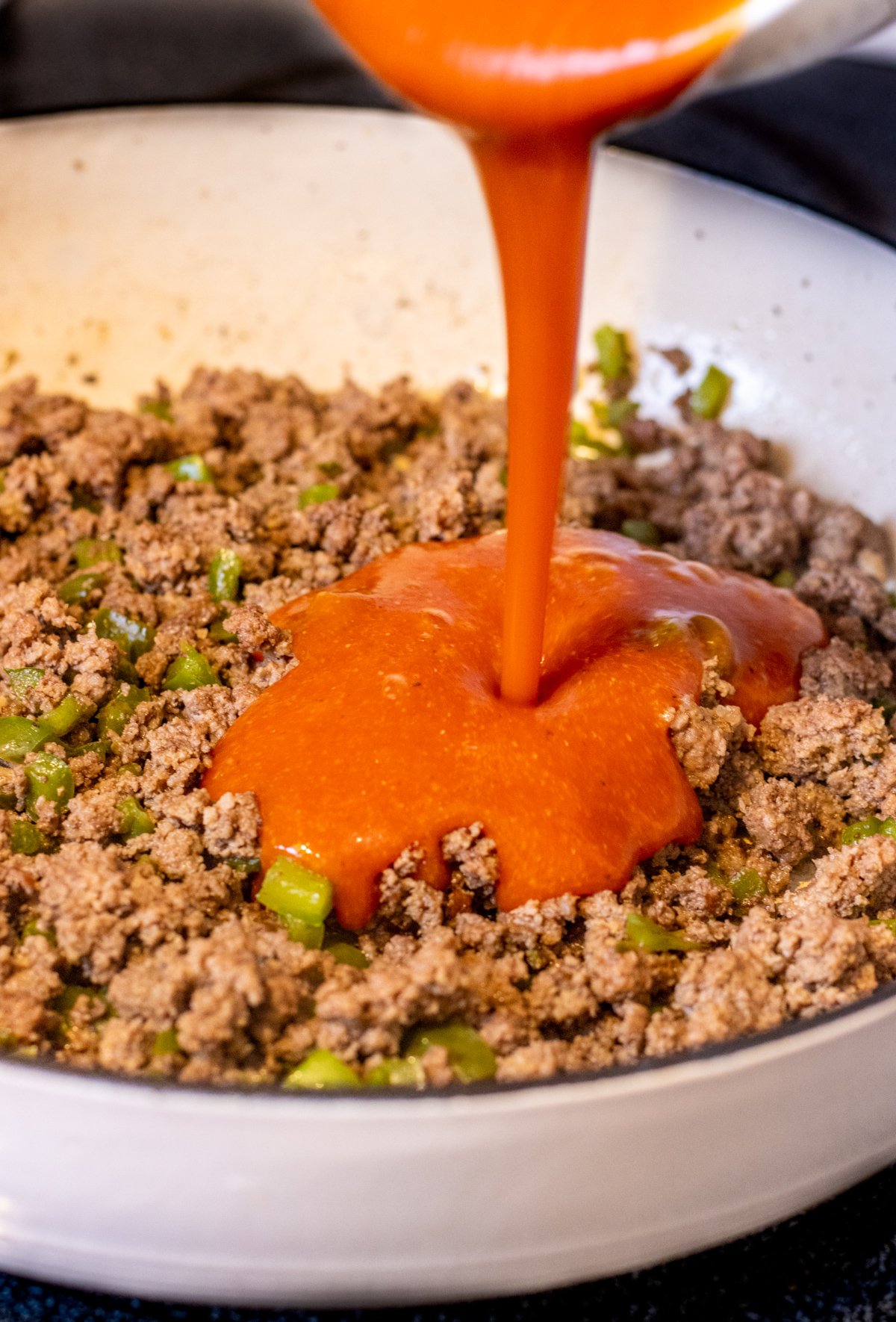 Sauce being poured into cooked ground beef.