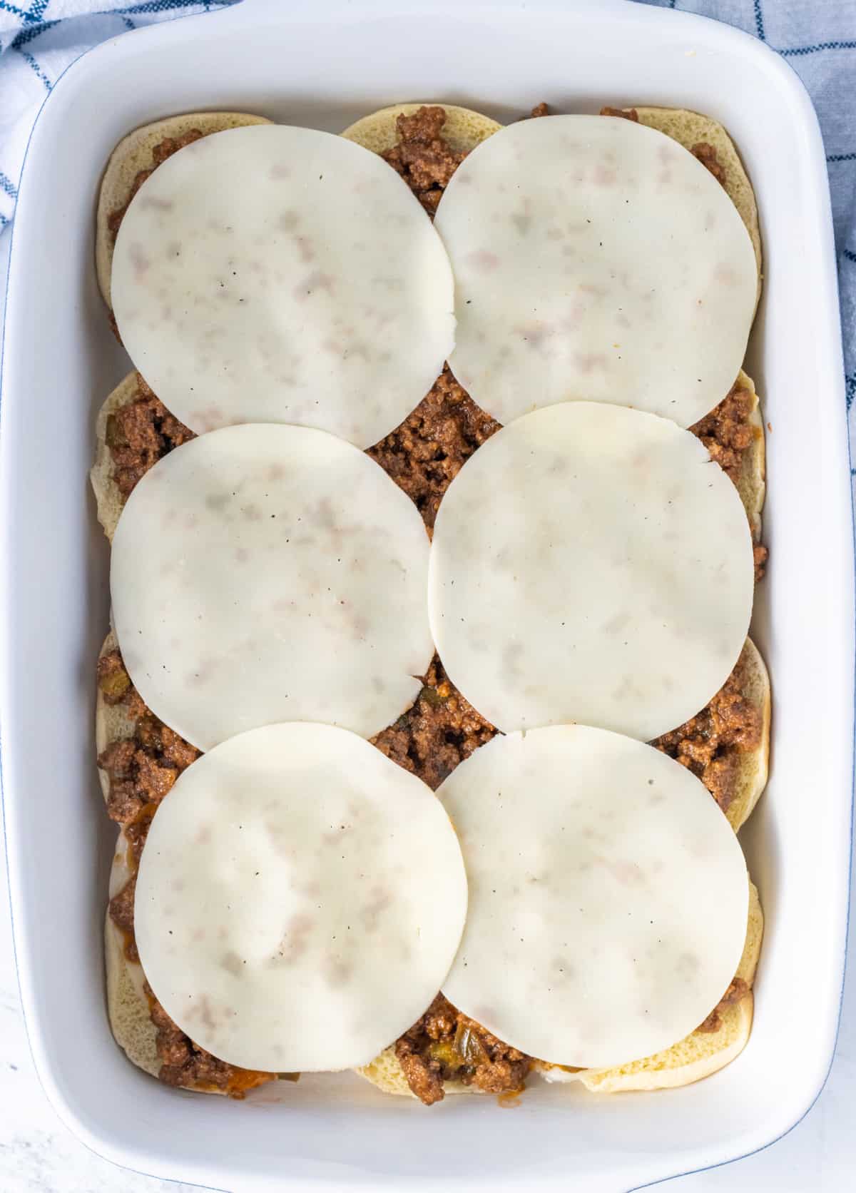 Slices of cheese on top of layers of sloppy joe meat, cheese, and the bottom buns.