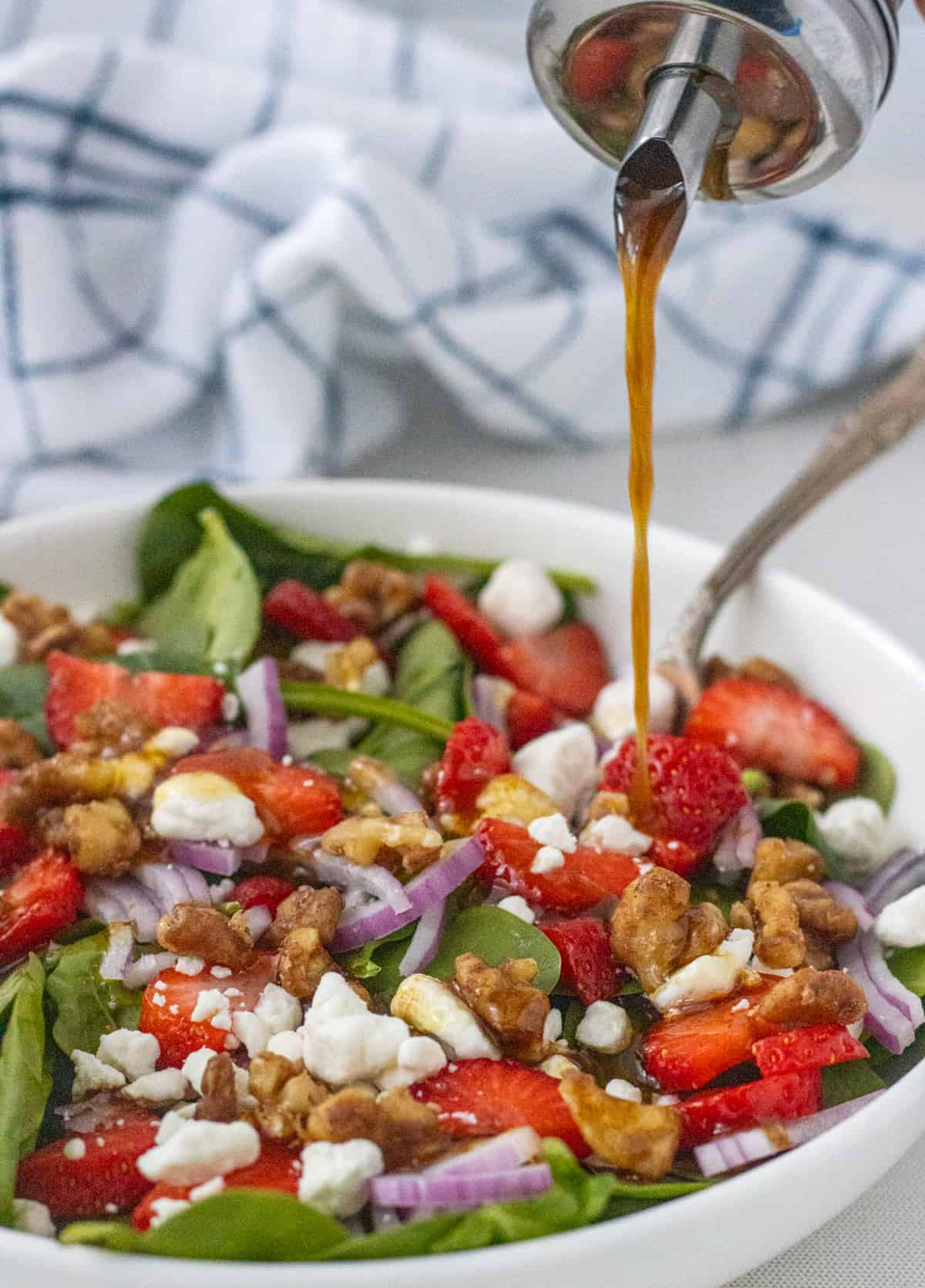 Strawberry goat cheese salad with balsamic dressing being drizzled over it.