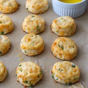 Cheddar jalapeno biscuits on a baking sheet with a bowl of melted butter.