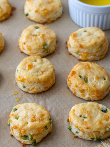 Cheddar jalapeno biscuits on a baking sheet with a bowl of melted butter.
