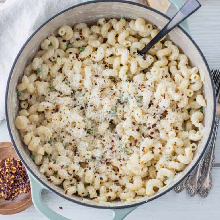 Pot of lemon ricotta pasta topped with grated parmesan cheese and red pepper flakes with a large spoon in it.