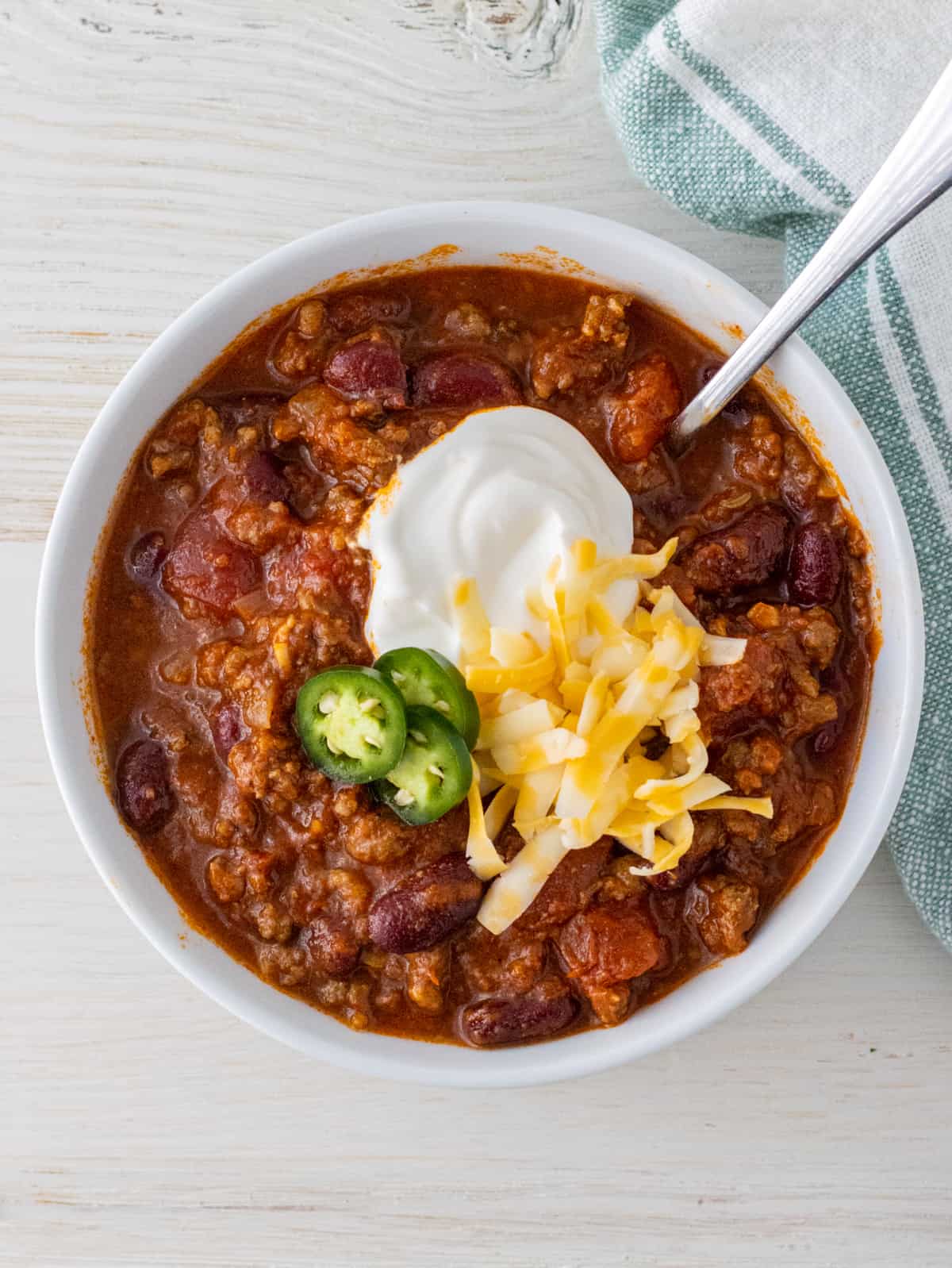 Bowl of chili topped with sour cream, shredded cheese, and jalapeno slices.