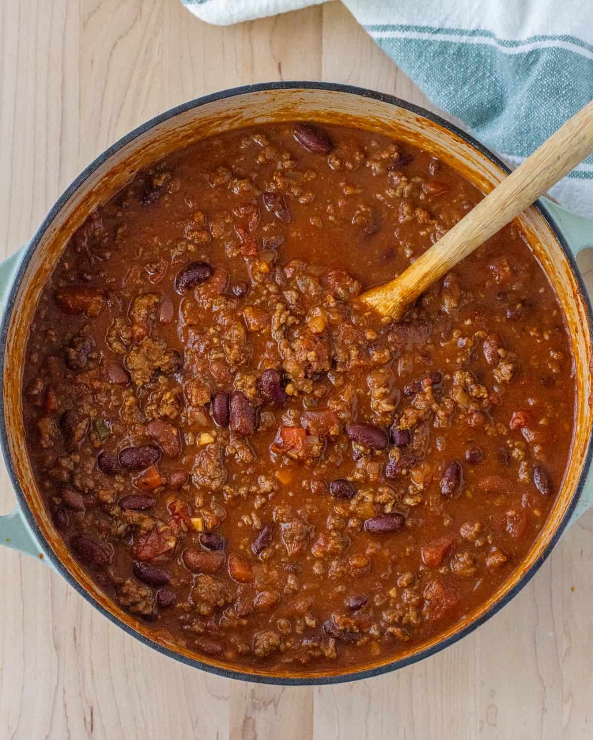Chili in a Dutch oven with a wooden spoon.