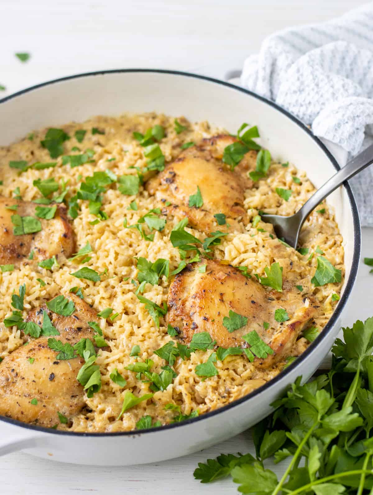 Chicken thighs and rice topped with chopped parsley in a casserole dish with a large spoon.