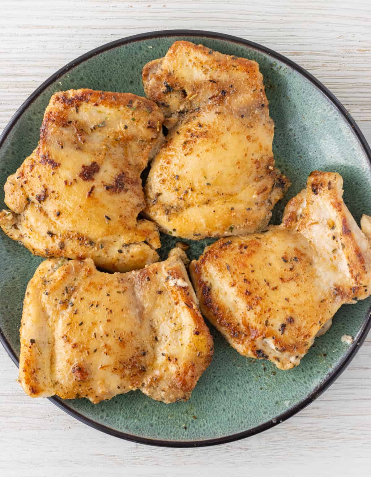 Four browned chicken thighs on a plate.
