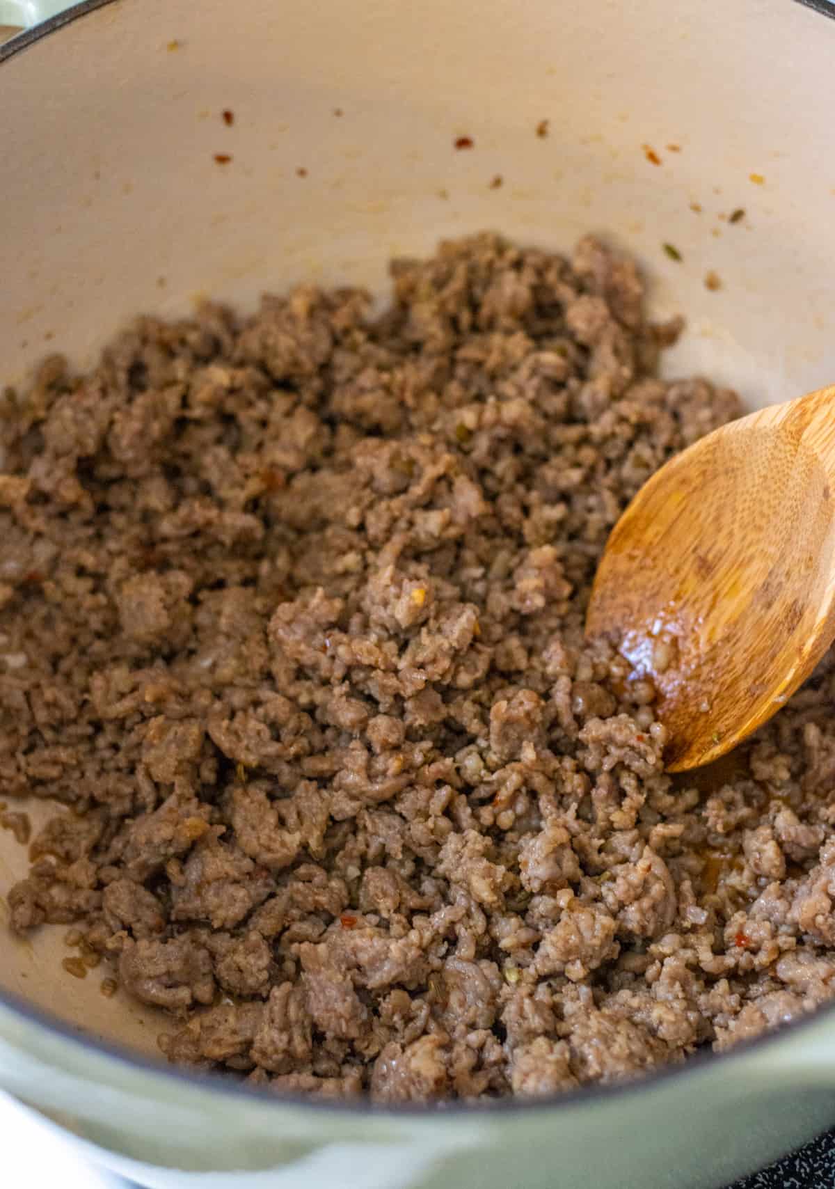 Cooked ground sausage in a pot with a wooden spoon.