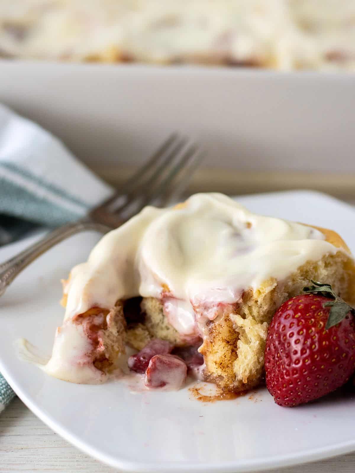 Strawberry cinnamon roll on a plate with a fork and a fresh strawberry.
