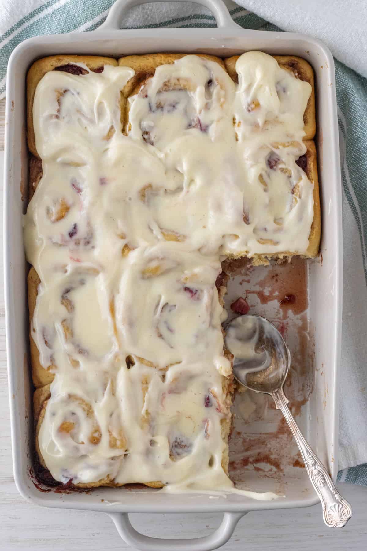 Strawberry cinnamon rolls in a baking dish with 2 missing and a spoon in the empty space.