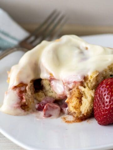 Strawberry cinnamon roll on a plate with a fork and fresh strawberry.
