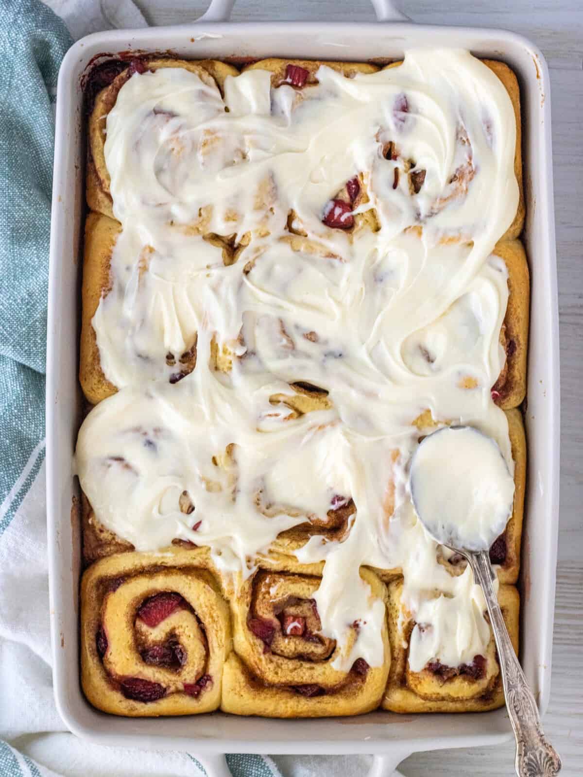 Strawberry cinnamon rolls in a 9x13 baking dish topped with frosting and a spoon.