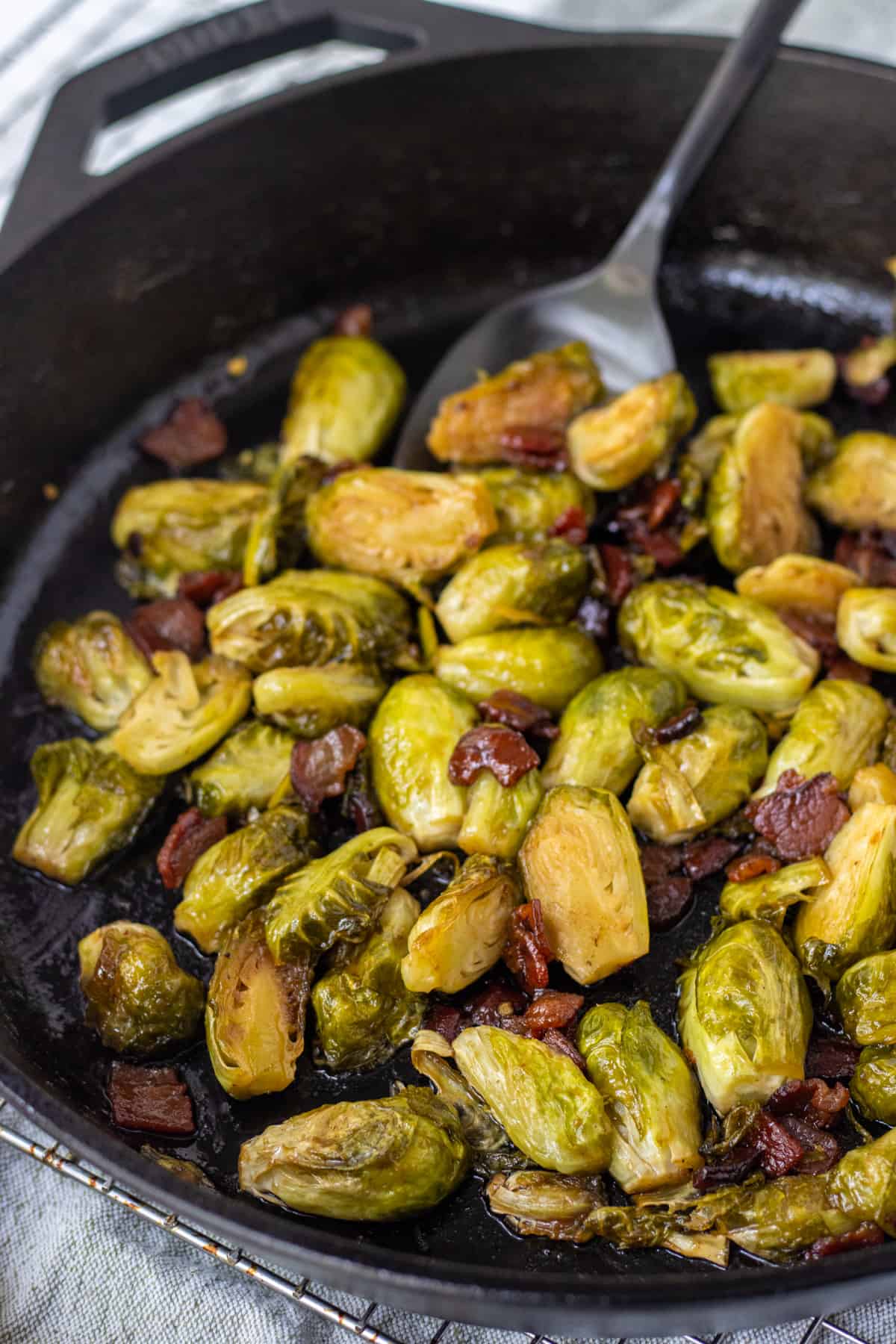 Caramelized Brussels sprouts and bacon in a cast iron skillet with a large spoon.