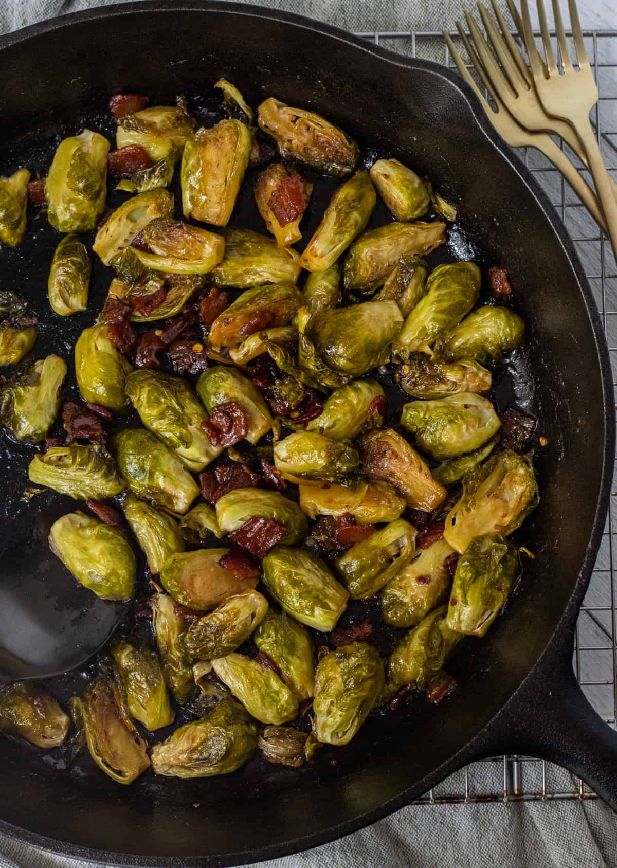 Caramelized Brussels sprouts in a cast iron pan over a wire rack next to forks.