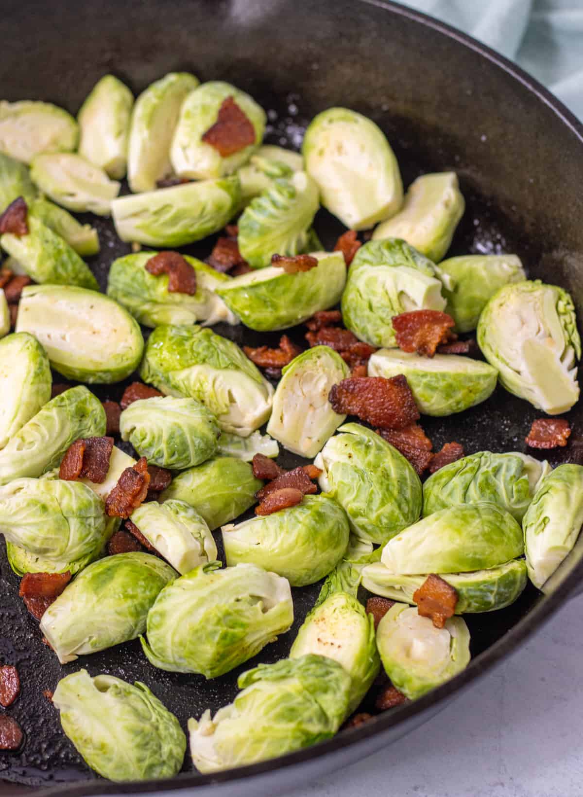Halved Brussels sprouts and bacon in a cast iron skillet.
