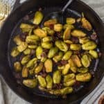 Caramelized Brussels sprouts and bacon in a cast iron skillet with a large serving spoon.