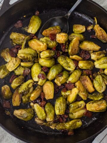 Caramelized Brussels sprouts and bacon in a cast iron skillet with a large serving spoon.