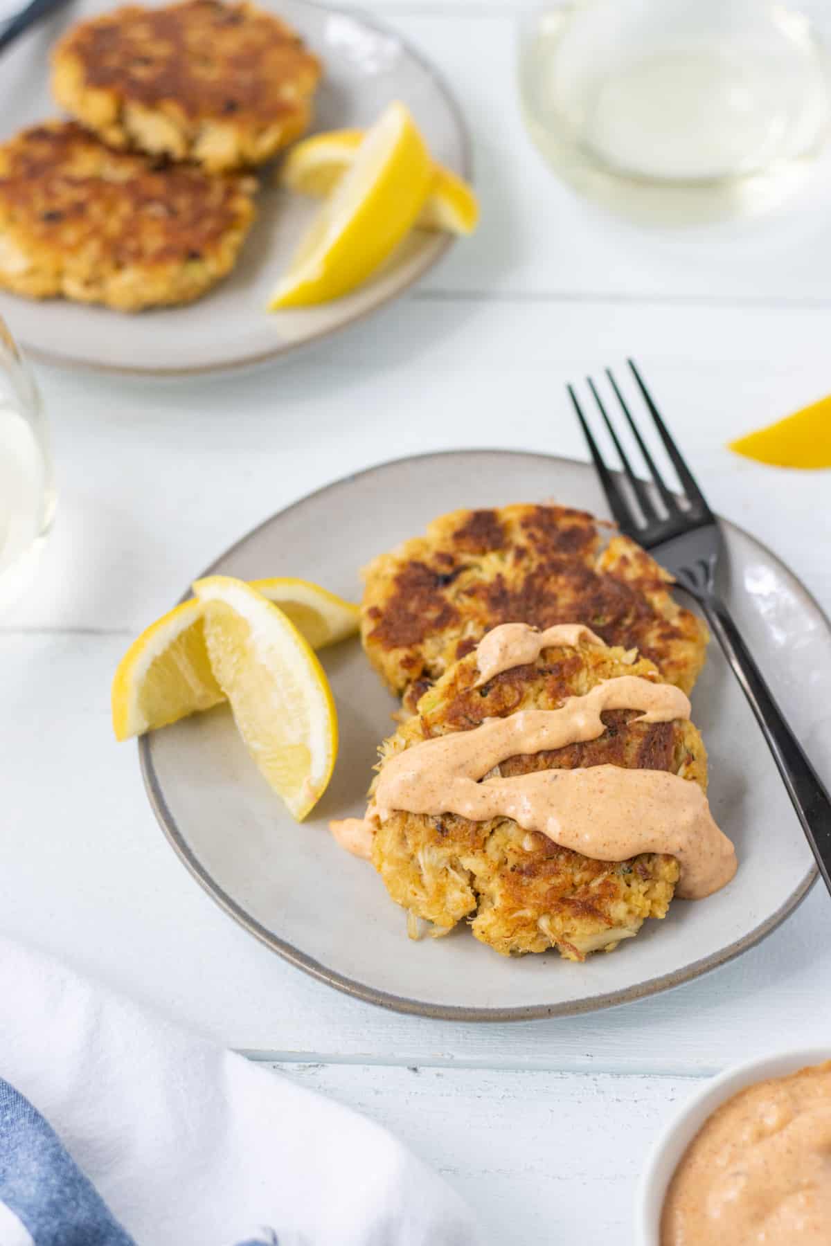 Crab cakes with remoulade sauce on them with lemon wedges.