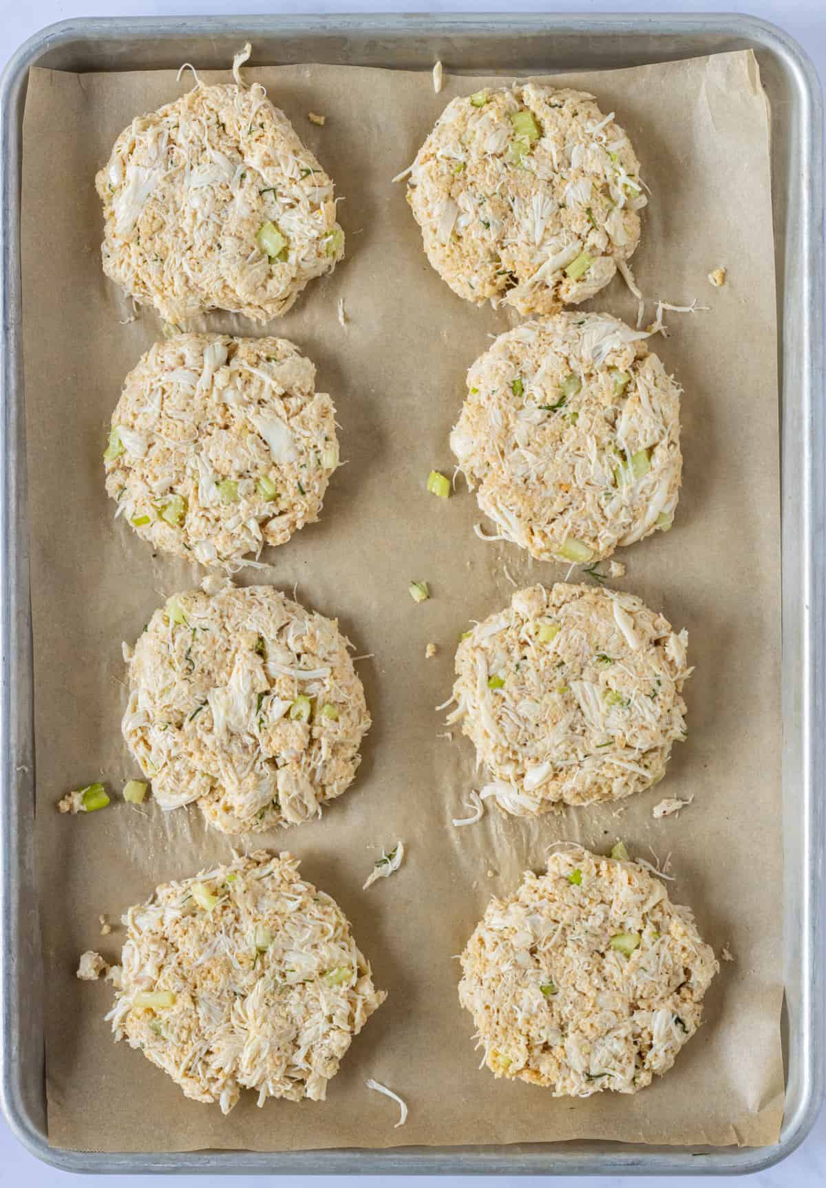 Uncooked crab cake patties on a parchment lined baking sheet.