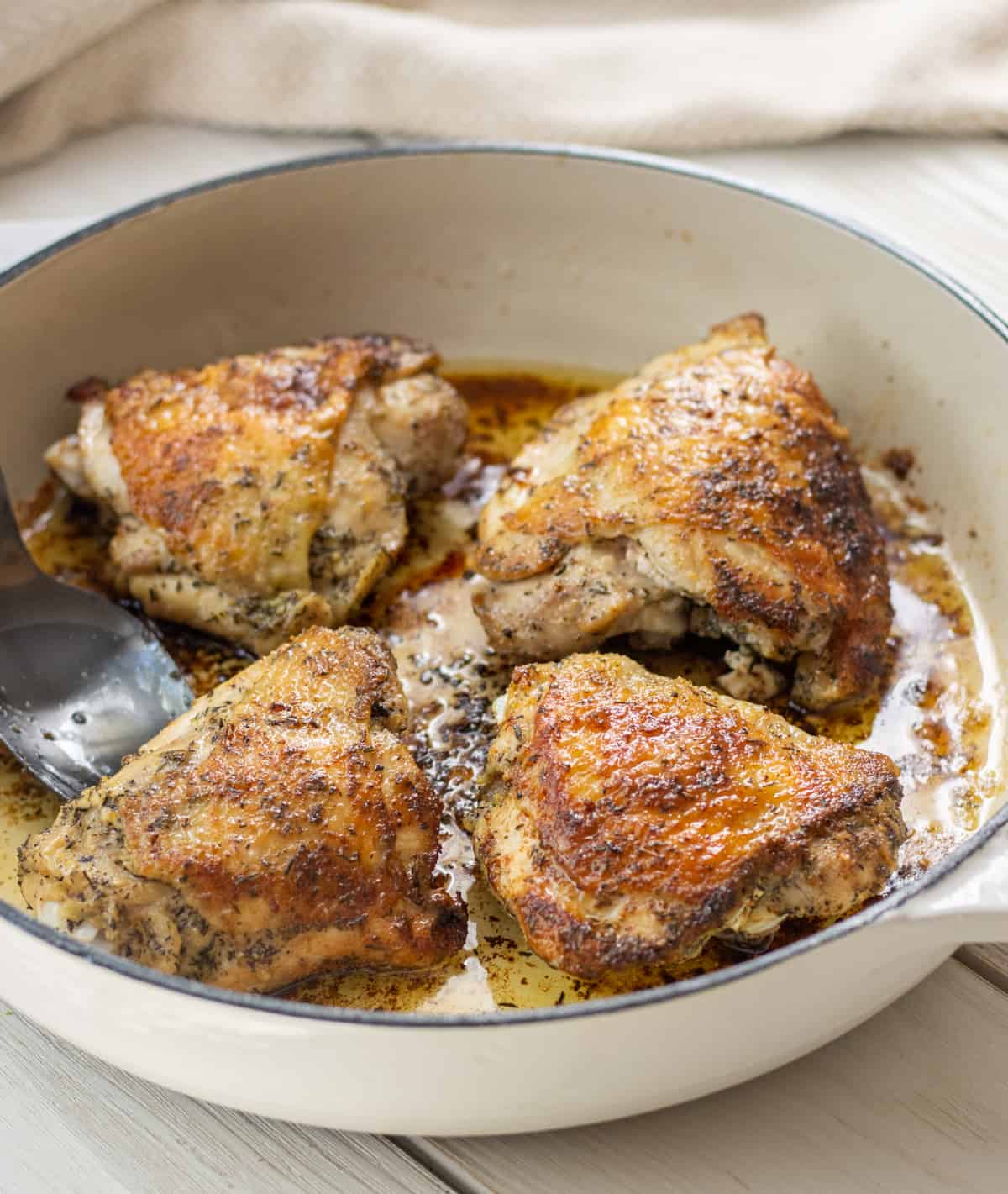 Four golden brown pan fried chicken thighs in a skillet.