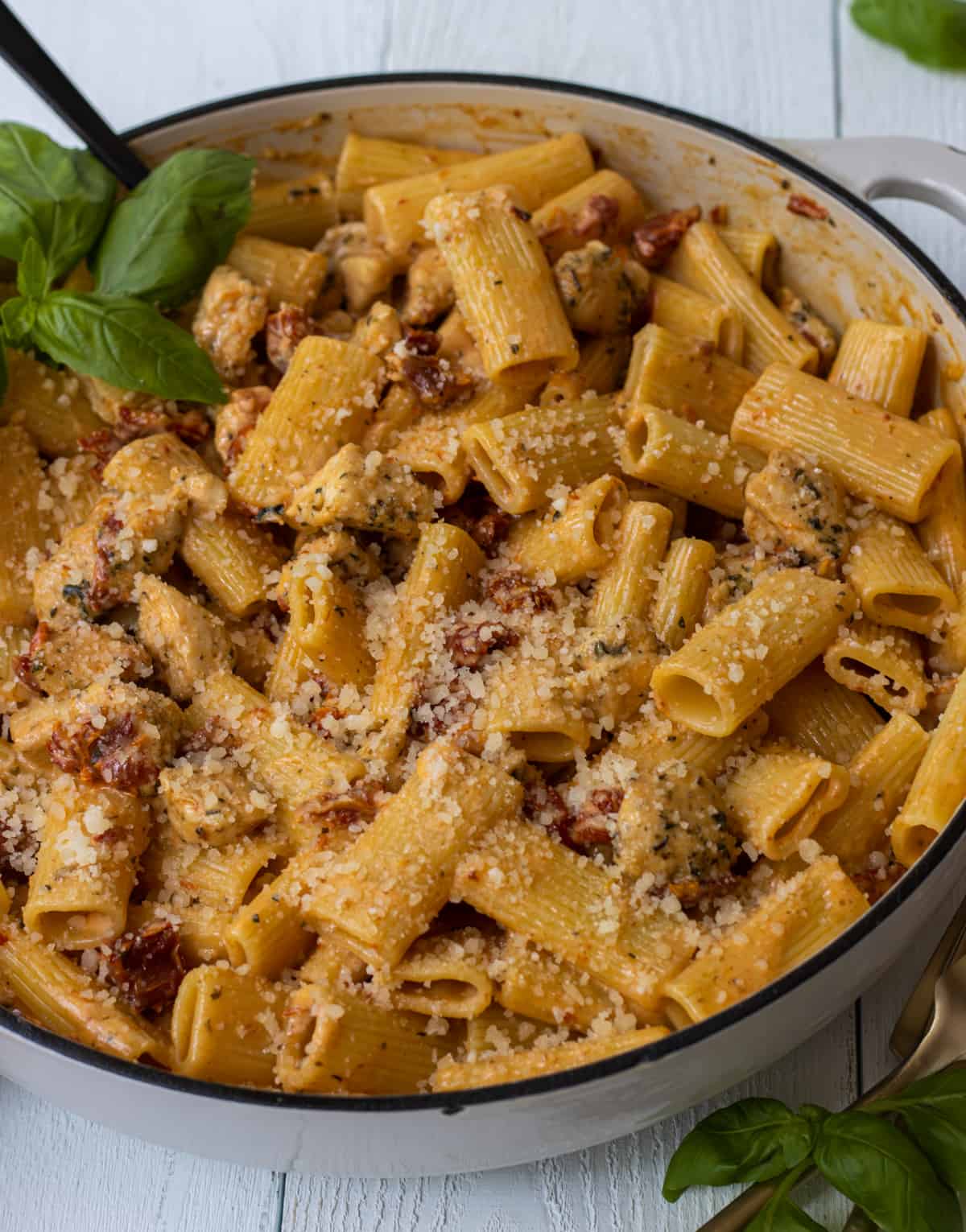 Sun-dried tomato chicken pasta with basil leaves and a large spoon.