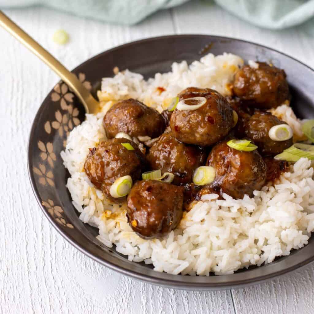 Sweet and spicy meatballs on white rice topped with slice green onion.