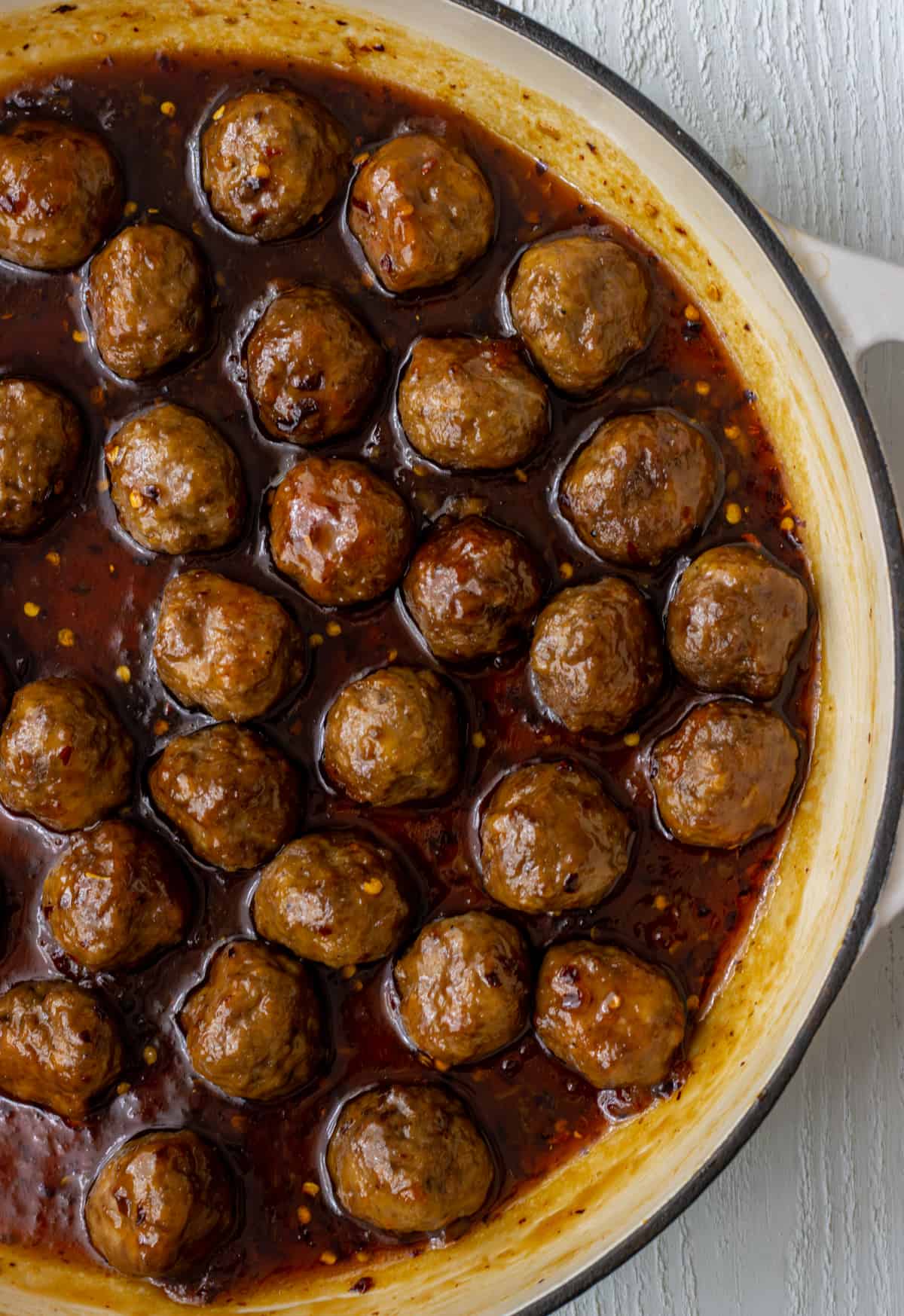 Meatballs coated in a sweet and spicy sauce in a skillet.