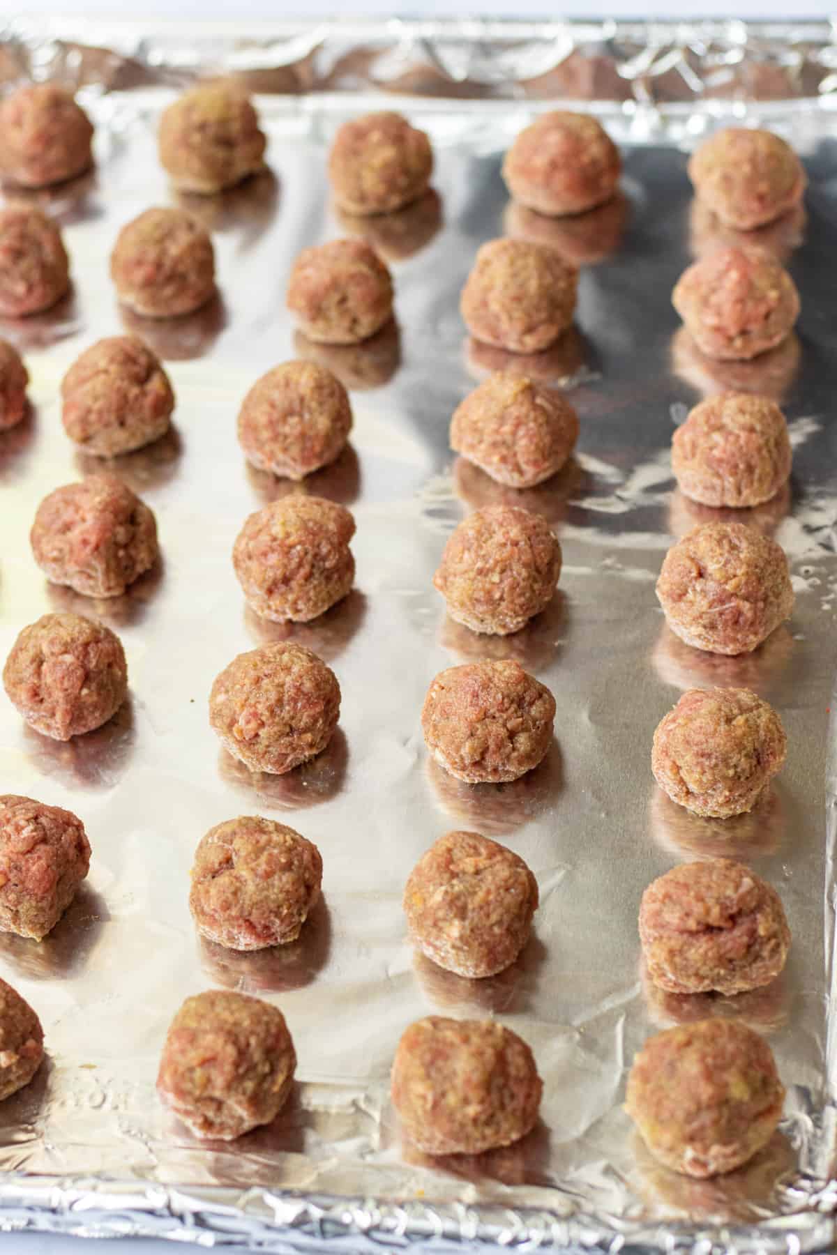 Unbaked meatballs on a foil-lined baking sheet.