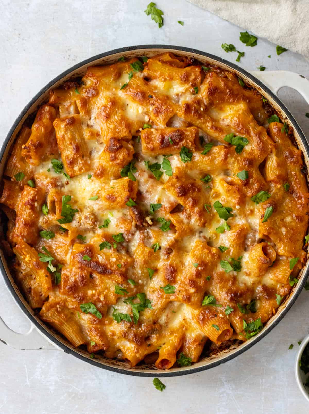 Baked rigatoni with sausage topped with chopped parsley in a skillet.