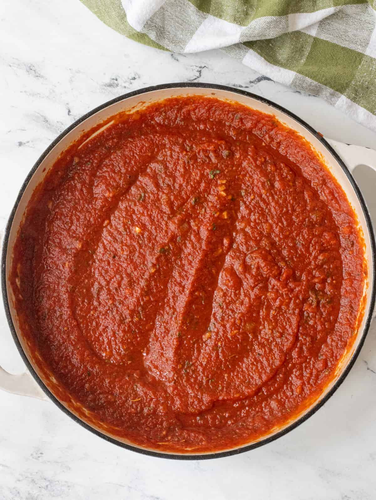Tomato sauce in a skillet next to a towel.