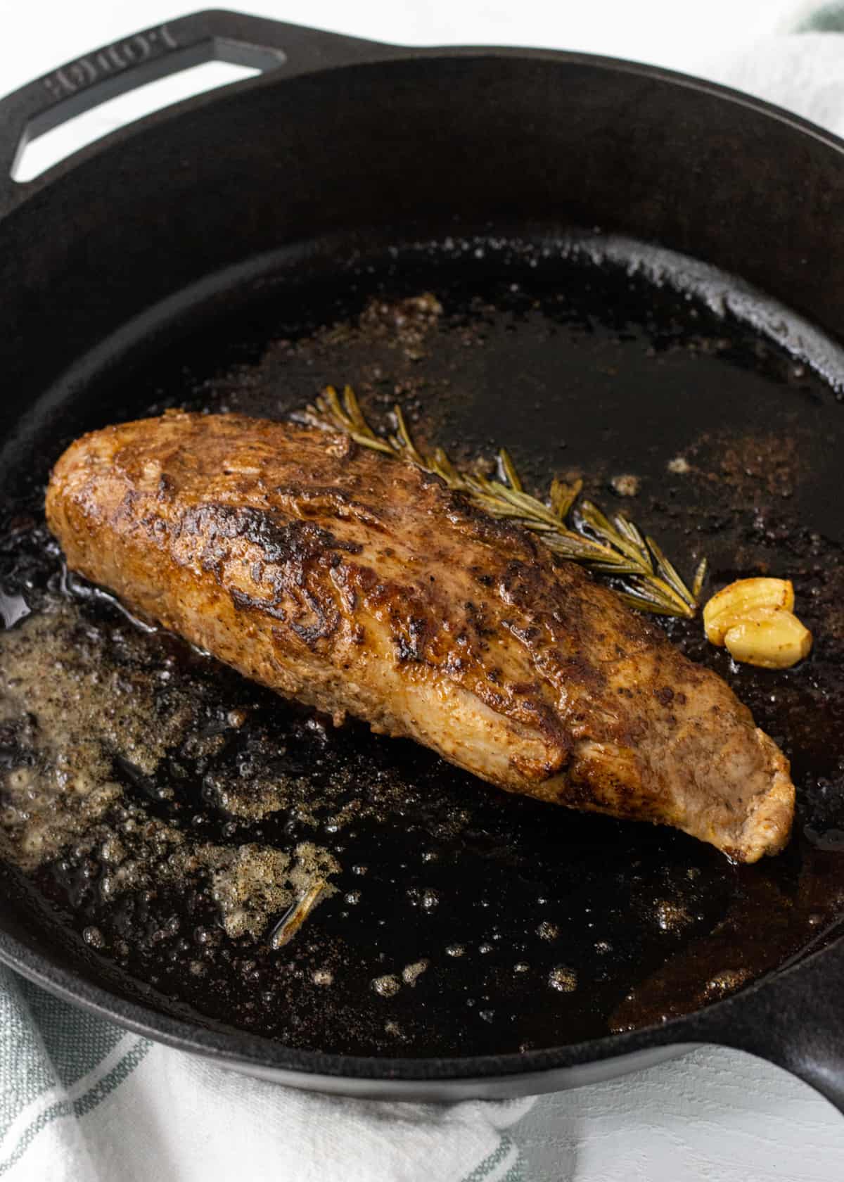 Roasted pork tenderloin in a cast iron skillet with a roasted sprig of rosemary and garlic clove.