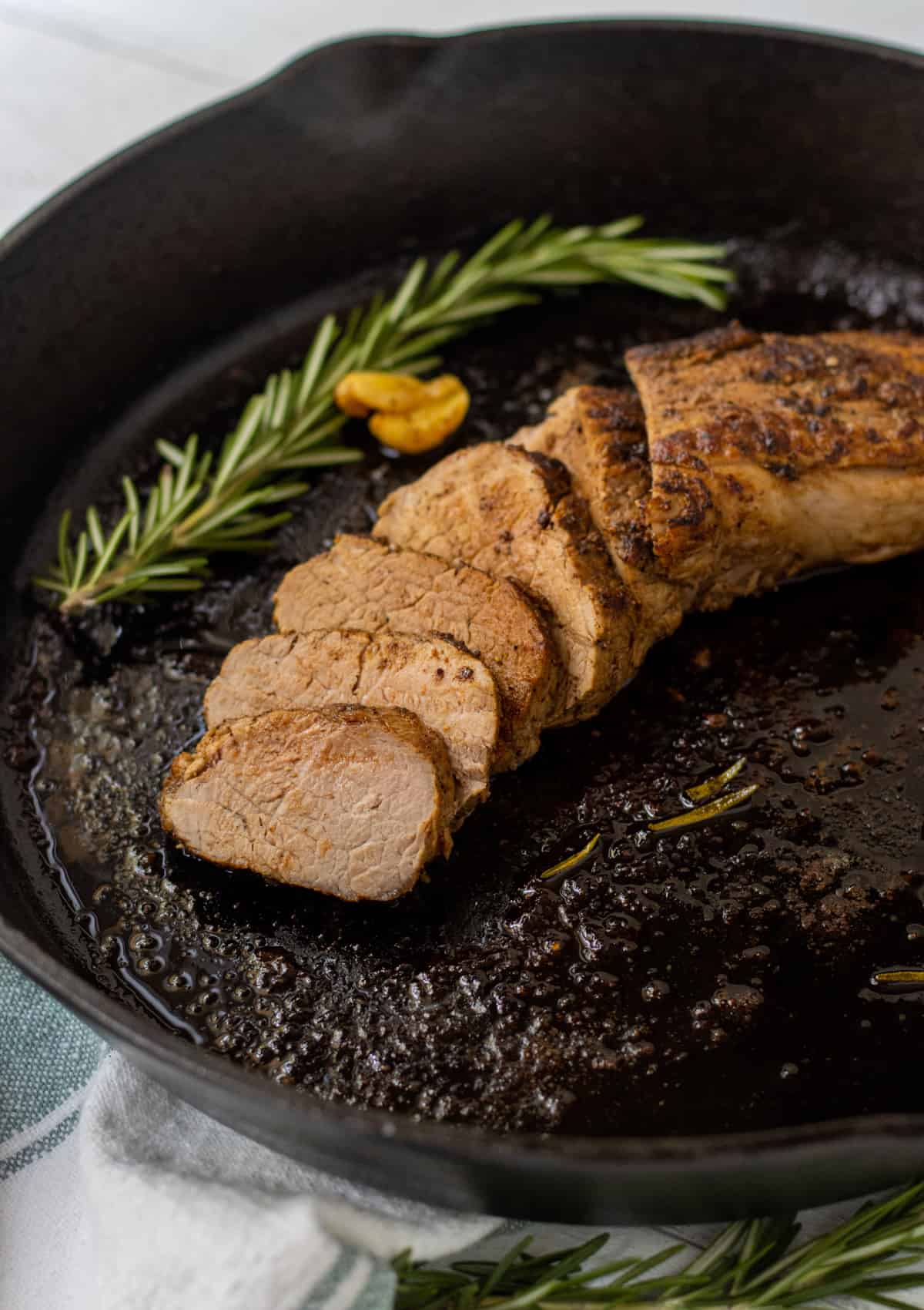 Sliced pork tenderloin in a cast iron skillet with rosemary and a garlic clove.
