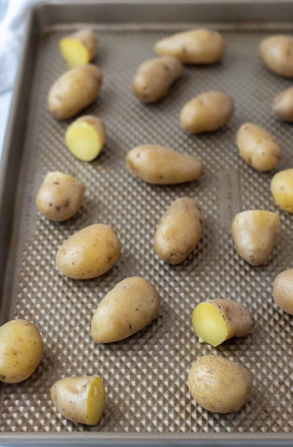 Boiled fingerling potatoes spread out on a baking sheet.