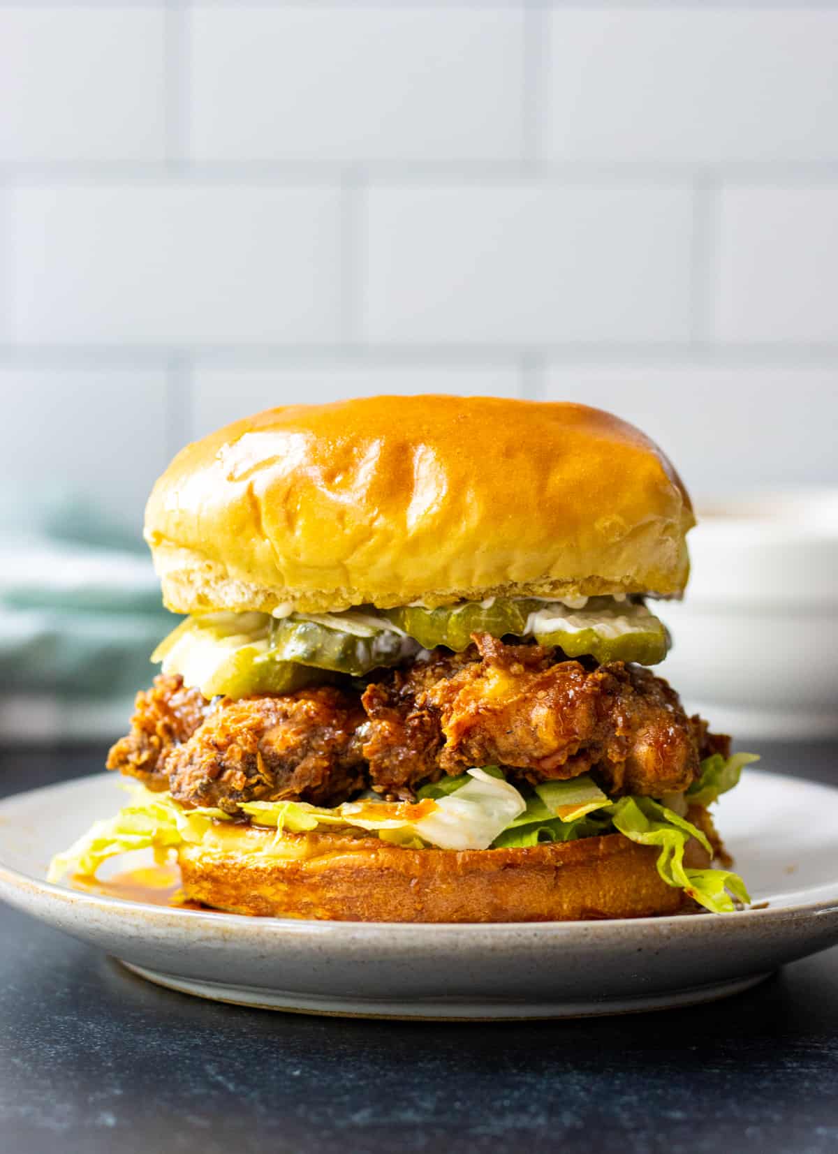 Hot honey chicken sandwich on a plate with a bowl and towel in the background.