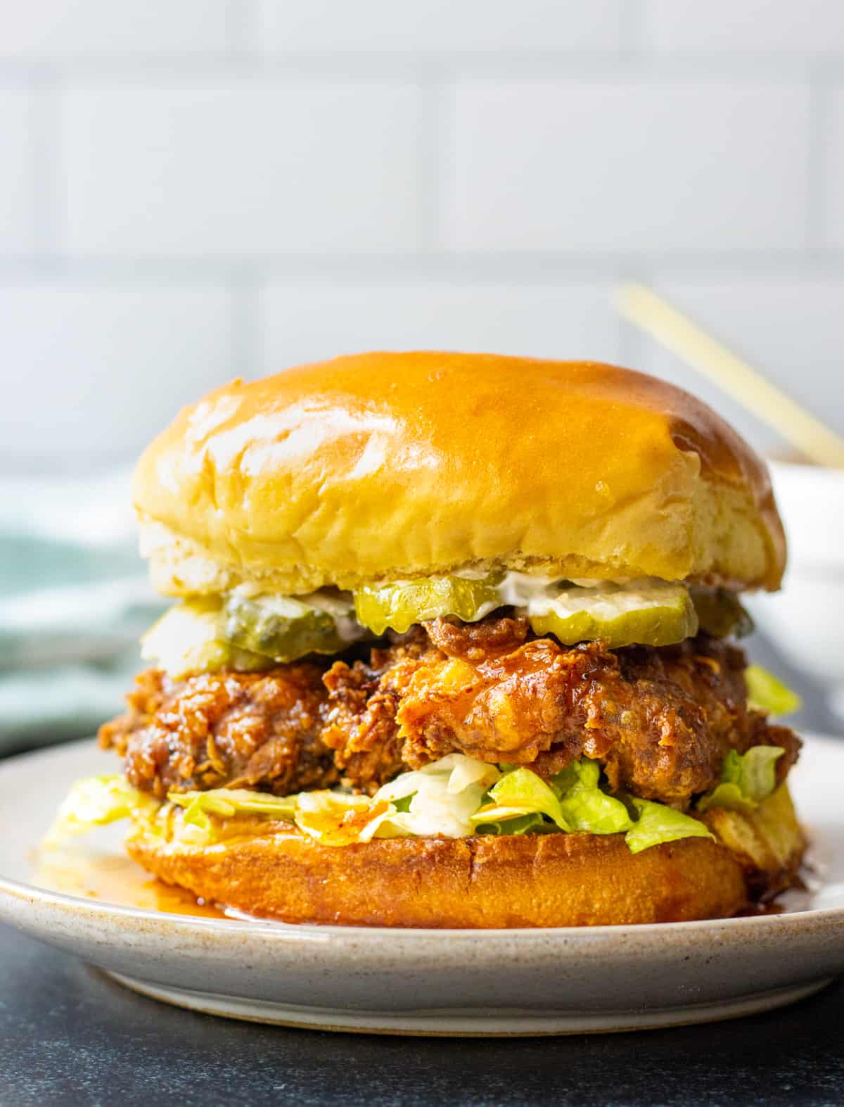Hot honey chicken sandwich with shredded lettuce and pickles on a plate.