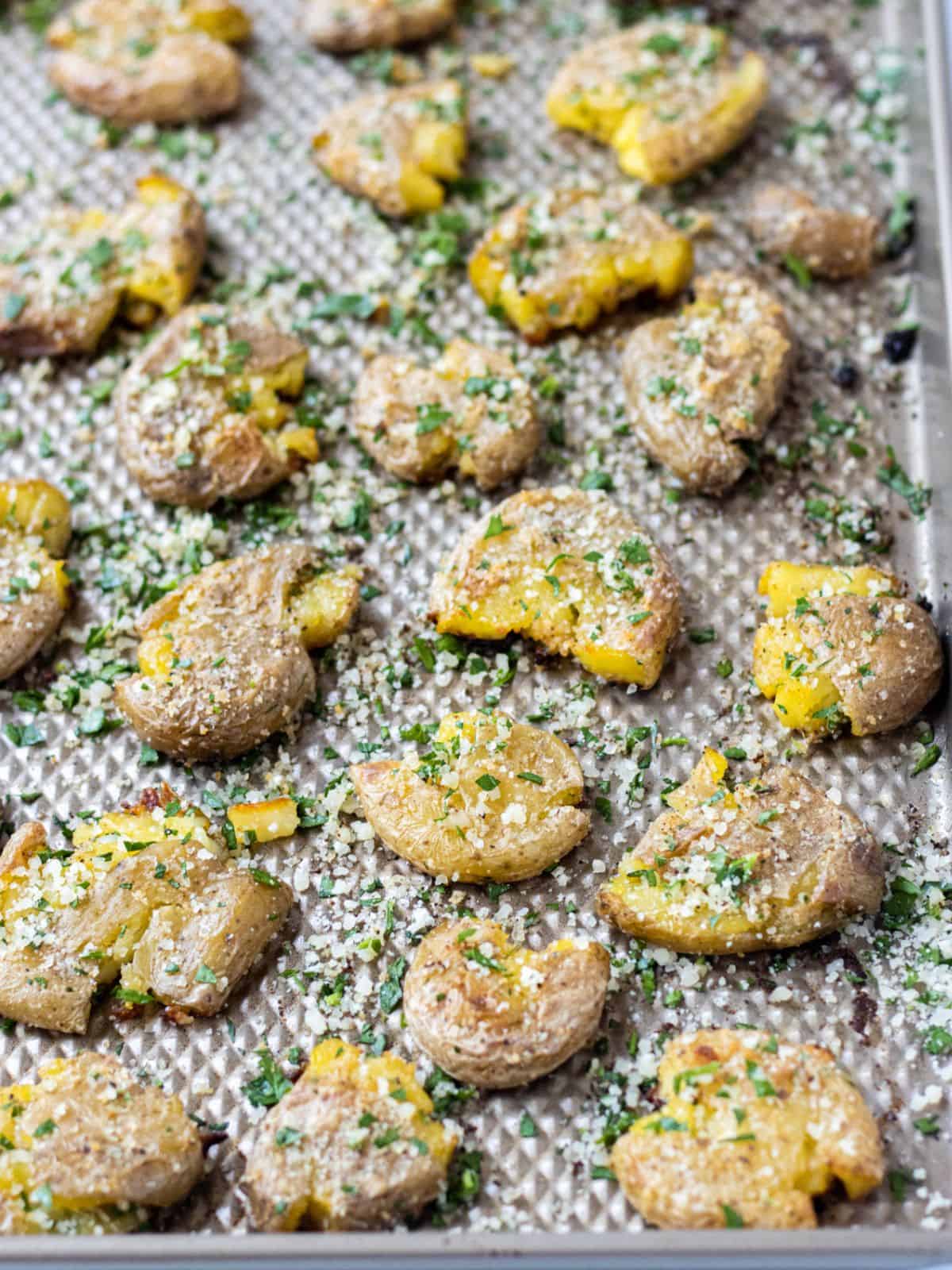 Smashed fingerling potatoes topped with parmesan and parsley on a baking sheet.