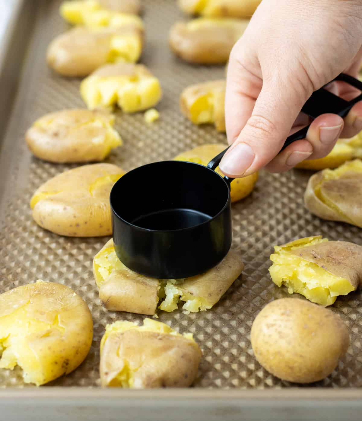 A hand holding a measuring cup pressed down on a fingerling potato.